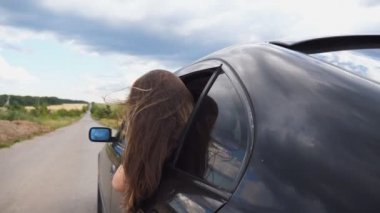 Güzel bir kadın araba camından sarkıyor ve kır yolunda giderken gezinin tadını çıkarıyor. Camdan dışarı bakan genç bir kız araba hareket ediyor ve uzun kahverengi saçları rüzgarda uçuşuyor. Yavaş çekim