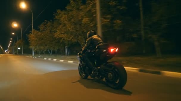 Человек едет на современном спортивном мотоцикле на ночной улице города. Мотоциклист гоняет на мотоцикле по вечернему городу. Парень за рулем велосипеда во время поездки. Концепция свободы и приключений. Вид сзади Закрыть — стоковое видео