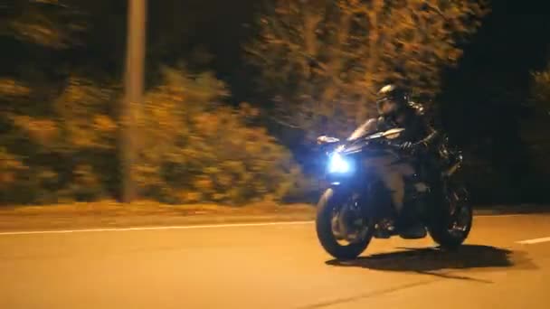 Молодой человек в шлеме быстро едет на современном черном спортивном мотоцикле на вечерней улице города. Мотоциклист гоняет на своем мотоцикле по ночной пустой дороге. Парень за рулем велосипеда. Понятие свободы и хобби. Закрыть — стоковое видео