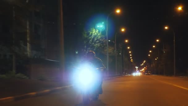 Mężczyzna jeżdżący na nowoczesnym sportowym motocyklu z włączonymi reflektorami w nocy. Motocyklista ściga się motocyklem po ciemnej ulicy. Facet jeżdżący rowerem podczas podróży. Pojęcie wolności i przygody. Widok z przodu — Wideo stockowe