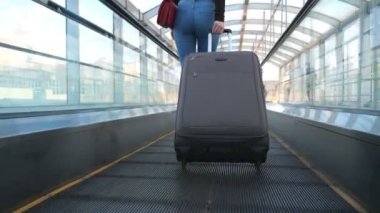 Yürüyen merdivende bavuluyla yürüyen tanınmayan genç bir kız. Seksi bir kadının bavulunu tekerlekli sandalyeyle çekmesi. Bayan tökezleyecek. Seyahat ya da tatil kavramı. Yavaş çekim Arka plan