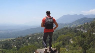 Sırt çantalı erkek yürüyüşçü dağın tepesine uzanır ve kollarını uzatır. Genç gezgin kanyonun kenarına koşar ve ellerini kaldırır. Erkek turistler güzel manzaranın tadını çıkarırlar.