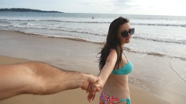 Následujte mě záběr krásné ženy v plavkách táhne jejího přítele k oceánu. Mladá dívka drží mužskou ruku a běží k moři. Letní dovolená nebo prázdninový koncept. Pohled POV Zpomalený pohyb — Stock video