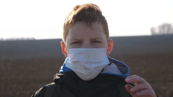 Porträtt av en liten pojke med medicinsk ansiktsmask stående utomhus. Glada manliga barn ta av skyddande mask från virus och leende. Begreppet hälsa och säkerhet på grund av coronavirus och pandemi — Stockvideo