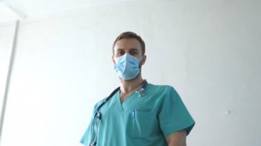Tıbbi maske takan beyaz erkek doktorun portresi kameraya bakıyor. Virüsten koruyucu maske takan bir tıp çalışanı. Koronavirüs salgınından sağIık ve güvenlik kavramı. COVID-19