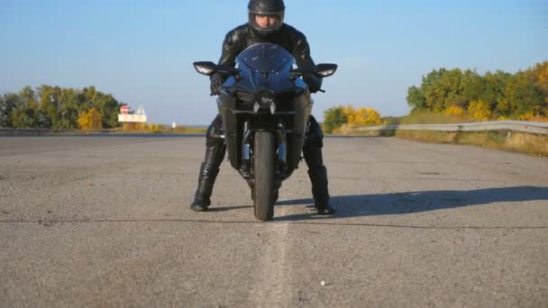 Vista frontal do jovem motociclista em capacete e jaqueta de couro está sentado na motocicleta na estrada da estrada e pronto para montar. O homem vai andar de mota desportiva. Conceito de liberdade e aventura. Fechar — Vídeo de Stock