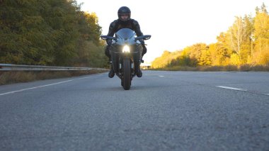 Motosikletli, kır yolunda motosikletiyle yarışıyor. Kasklı genç adam otoyolda modern spor motosikletle hızlı gidiyor. Yolculuk sırasında bisiklet süren adam. Macera kavramı. Ön görünüm Kapat.