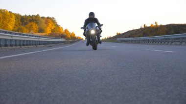 Kasklı bir gencin modern spor motosikletle otobanda süratle sürüşünü ön planda görüyoruz. Motosikletli, kır yolunda motosikletiyle yarışıyor. Yolculuk sırasında bisiklet süren adam. Özgürlük ve macera kavramı.