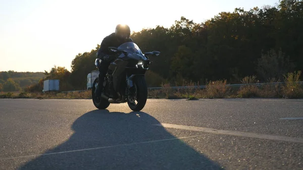 戴头盔的男子骑着现代摩托车在高速公路上飞驰而去 背景是太阳耀斑 骑摩托车的人在乡间路上骑摩托车 旅行时骑自行车的家伙 自由的概念 — 图库照片