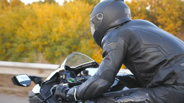 Autumn Country Road 'da motosikletle yarışan motosikletlilere yaklaş. Kasklı genç adam otoyolda modern spor motosiklet kullanıyor. Yolculuk sırasında bisiklet süren adam. Özgürlük ve macera kavramı.