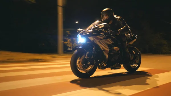 Miğferli genç adam şehir caddesinde modern siyah spor motosikletle hızlı gidiyor. Motosikletli, boş yolda motosikletiyle yarışıyor. Bisikletli adam. Özgürlük ve hobi kavramı. Kapat..