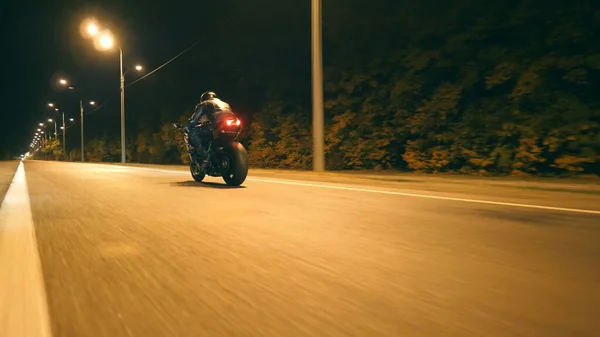 Night City caddesinde, modern motorsikletle hızlı giden bir adam. Motosikletli, boş yolda motosikletiyle yarışıyor. Alacakaranlıkta bisiklet süren adam. Özgürlük ve macera kavramı. Düşük açı. Yakın plan..