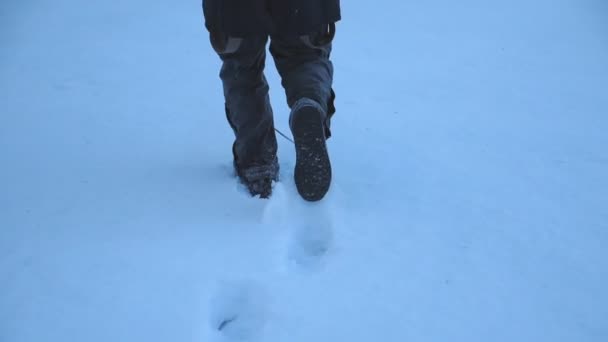 傍晚时分，雄性脚在大雪中行走时的后视镜。一个难以辨认的家伙在冬天的旅行中享受着自由。假期或假日的概念。特写慢动作 — 图库视频影像