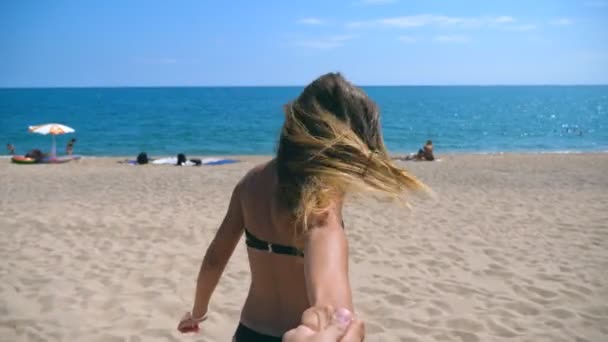 Sígueme la foto de una joven mujer que lleva a su novio a la orilla del mar. Hermosa chica sosteniendo la mano masculina y corriendo en la playa del complejo al océano. Vacaciones de verano o vacaciones. Punto de vista POV Cámara lenta — Vídeo de stock