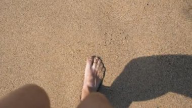 Genç bir adamın deniz sahilindeki altın kuma adım atması. Erkek bacakları okyanus kenarında yürüyor. Dalgalarla kumlu kıyıya çıkan çıplak ayaklı bir adam. Yaz tatili ya da tatil Yavaş çekim POV 'u kapat