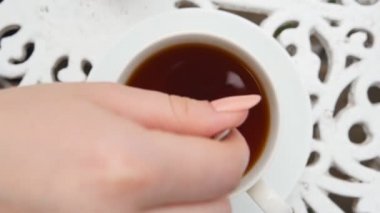 Kadın eli metal kaşığı tutuyor ve beyaz bir fincanda şeker ya da Stevie 'yi bitki çayıyla karıştırıyor. Genç bayan kahvaltıda sağlıklı sıcak içecek hazırlar. Sükunet ve rahatlama kavramı. Üst Görünüm Yavaş Çekim