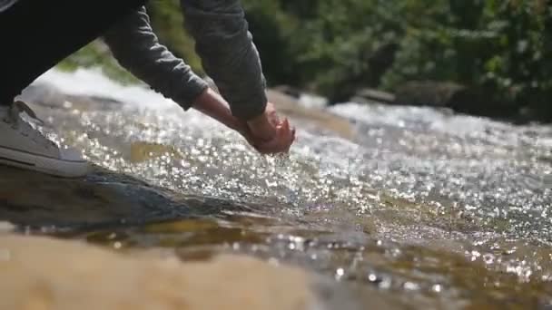 Young female hiker washes her hands in clear water of mountain river. Unrecognizable woman refreshes her arms with cold aqua in forest lake. Concept of adventure or journey. Low view Slow motion — Stock Video
