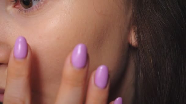 Mujer joven que aplica crema en la cara. Chica bonita cuidando de sí misma haciendo maquillaje usando cosméticos. Modelo atractivo en salón de belleza. Concepto de moda y estilo. Vista detallada Primer plano — Vídeo de stock