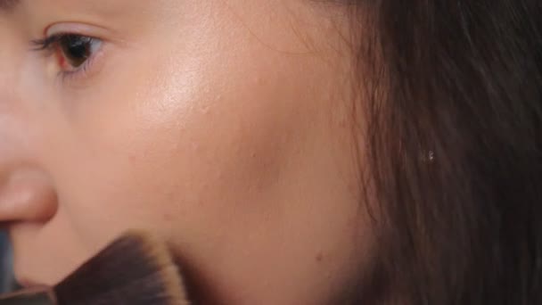 Mujer joven que aplica cosméticos en la cara con un cepillo grande. Una chica guapa cuidando de sí misma maquillándose. Modelo atractivo en salón de belleza. Concepto de moda y estilo. Vista detallada Primer plano — Vídeos de Stock