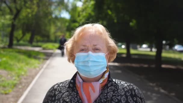 Na ulicy miejskiej stoi portret staruszki w masce medycznej. Szczęśliwa babcia zdejmuje maskę ochronną przed wirusem COVID-19 i uśmiecha się. Koncepcja bezpieczeństwa i higieny pracy w przypadku pandemii koronawirusowej — Wideo stockowe