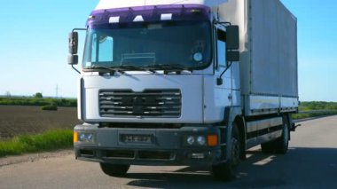 Kamera, kargo karavanıyla otoyolda giden ve yaz günü malları taşıyan kamyonu takip ediyor. Arka planda doğa manzarası olan bir kamyon. Yavaş çekim Ön görünüm Kapat