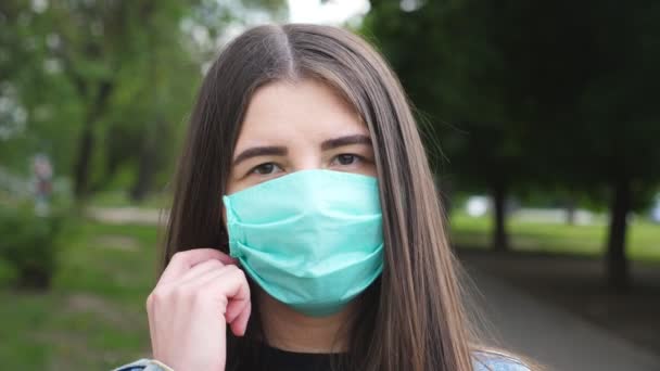 Retrato de mujer joven y feliz se quita la mascarilla médica y sonríe. Chica elimina la máscara protectora del virus COVID-19 al aire libre. Concepto de la vida de salud y seguridad de la pandemia de coronavirus. De cerca. — Vídeos de Stock