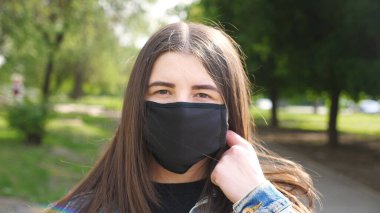 Mutlu genç bir kadının portresi siyah maskesini çıkarır ve gülümser. Kız dışarıdaki COVID 19 virüsünden koruyucu maskeyi çıkarıyor. Koronavirüs salgınından sağIık ve güvenlik kavramı. Kapat.