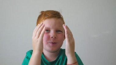 Sevimli, kızıl saçlı, çilli bir çocuk kameraya bakıyor ve el kaldırıyor. İçindeki başarıyı alkışlıyor. Yüzünde mutluluk ve sevinç duyguları olan mutlu genç bir çocuğun portresi. Yavaş çekim