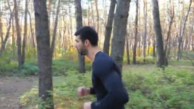 Arka planda manzarası olan genç bir adam ormanda koşuyor. Atletizm ve açık havada egzersiz. Sportif adam tahtada kardiyo çalışması yapıyor. Sağlıklı aktif yaşam tarzı kavramı. Yan görünüm