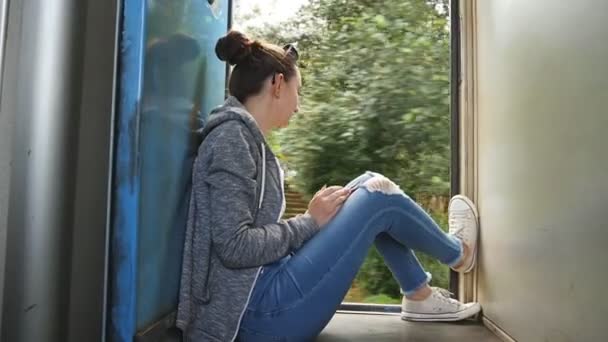 Jeune femme assise près des portes ouvertes du train en mouvement et regarde la belle nature. Promenades touristiques féminines sur le transport ferroviaire de passagers et apprécie les voyages d'été. Concept de vacances ou de vacances — Video