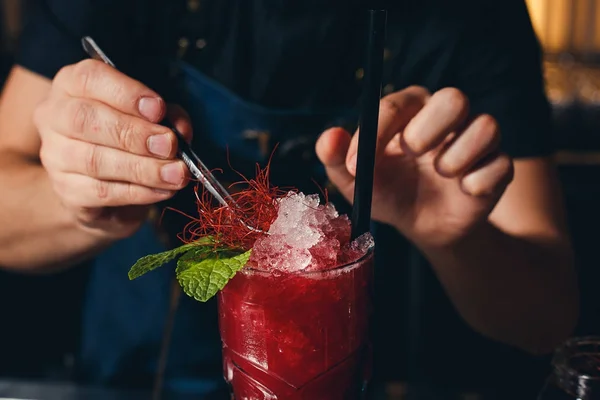 Barkeeper Hände, die den Saft in das mit alkoholischen Getränken gefüllte Cocktailglas auf dem dunklen Hintergrund streuen — Stockfoto