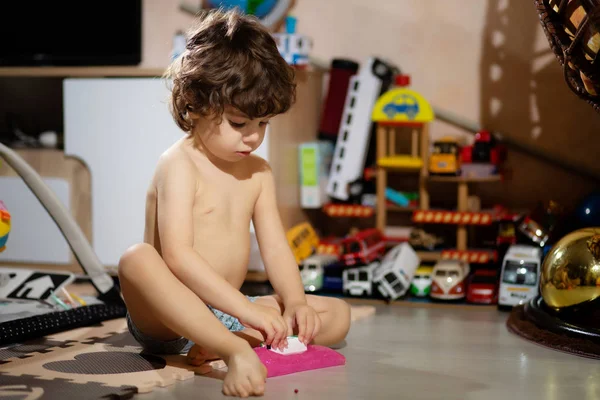 Curly-haired little boy in shorts plays with slime in his room, so as not to get his clothes dirty. — Stock Photo, Image