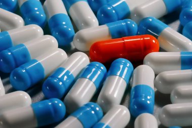 Macro, farklı mavi beyaz ilaçlarla çevrili yalnız kırmızı bir kapsülü yakından çek. Yalnızlık kavramı