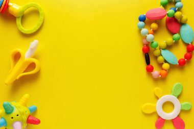 Sarı arka plandaki bebekler için renkli ve çeşitli plastik oyuncaklar. Yerleşim planı. Metin için boş alan. Minimalizm.