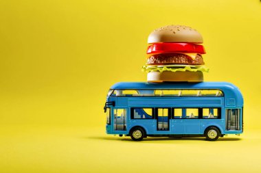 Mavi oyuncak otobüs sarı arka planda yiyecek burger dağıtıyor.
