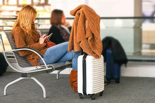 White color suitcase and beautiful woman looking at cellphone, in airport.