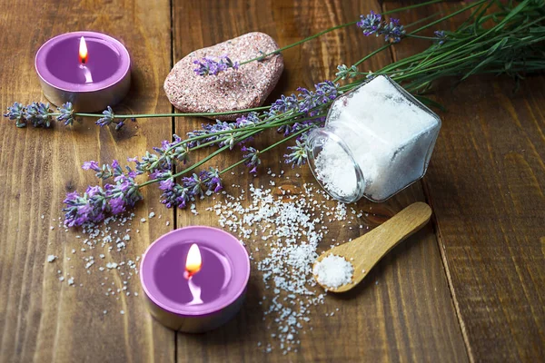 Spa massage setting with lavender flowers, scented aroma candles and cosmetic salt on wooden background. — Stock Photo, Image