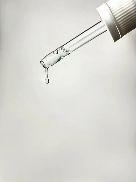 Pipette with drop of serum or hyaluronic acid on gray background.