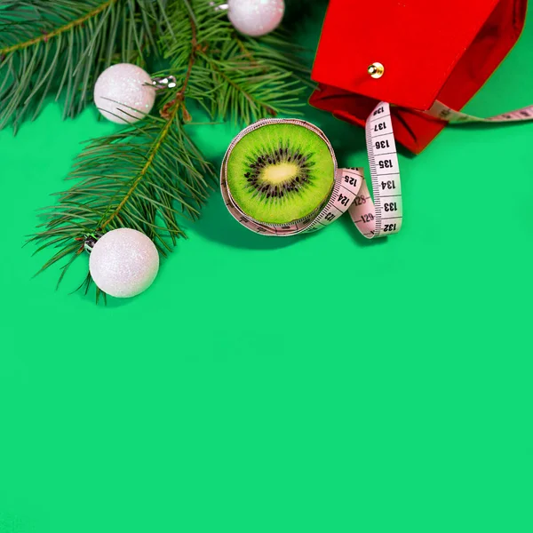 Concepto Vacaciones de Navidad dieta y estilo de vida saludable kiwi y cinta métrica con bolsa de regalo roja sobre fondo azul verde de moda . — Foto de Stock