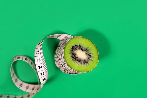 Concept diet and healhty lifestyle - kiwi and tape measure on trendy green blue background. — Stock Photo, Image