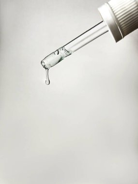 Pipette with drop of serum or hyaluronic acid on gray background. clipart