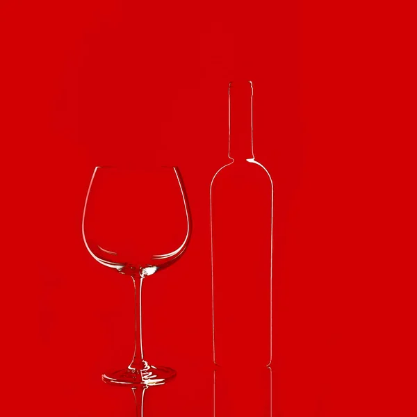 Boş şarap kadehi ve kırmızı arka planda izole edilmiş bir şişe.. — Stok fotoğraf