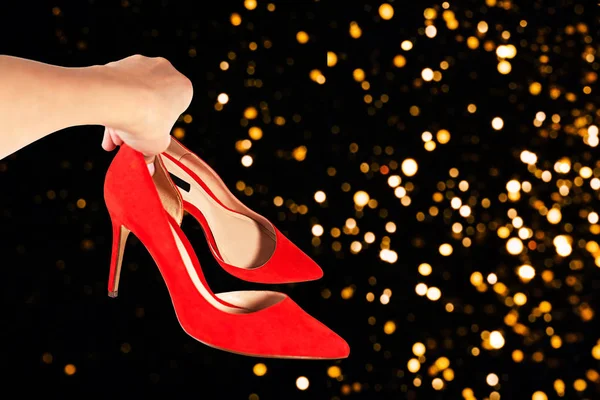 Wanita memegang sepatu merah modis di tangannya dengan latar belakang pesta Natal abstrak yang tidak terfokus . — Stok Foto