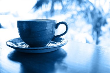 Tropikal arka planda bir fincan kahve, klasik mavi renkte..