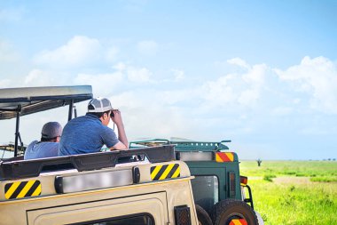 Tropikal safaride turistik araçtan dürbünle bakan adam..