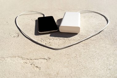 Güç bankası somut arka planda kalp şeklinde modern akıllı telefonu şarj ediyor.