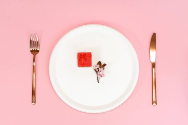 Bahar kiraz çiçeği ve krem rengi tabağın üstünde kırmızı hediye kutusu, bıçak ve çatal..