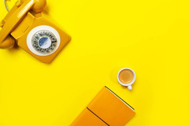 Geri dönüşümlü telefon, bir fincan kahve ve defter içeren sarı bir düzen..