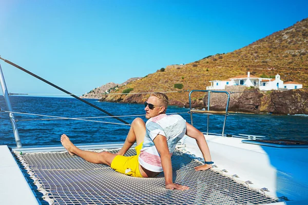 Happy young man feels happy on the luxury sail boat yacht catamaran in turquoise sea in summer holidays on island.