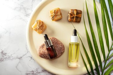 Cam üzerinde bitkisel yağ şişeleri aroma damlası ve pastel bej plaka üzerinde palmiye yaprağı ve mermer arka plan.